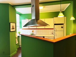 Una cocina con paredes verdes, encimera de madera, campana extractora de acero inoxidable, refrigerador blanco y lámparas colgantes.