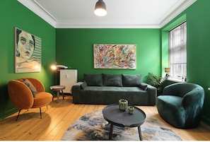 Una sala de estar con pared verde, un sofá, dos sillones, una mesita de centro y un cuadro.