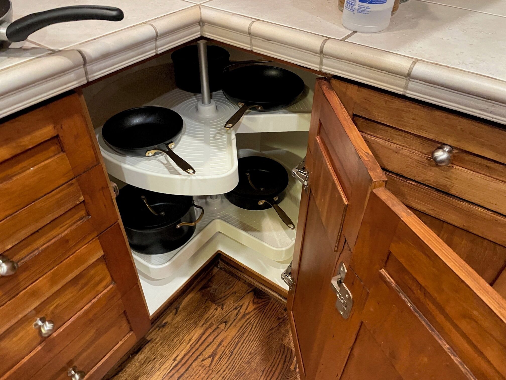 Cucina angolare con mobili in legno, piano di lavoro bianco e piano cottura integrato con pentole e padelle.