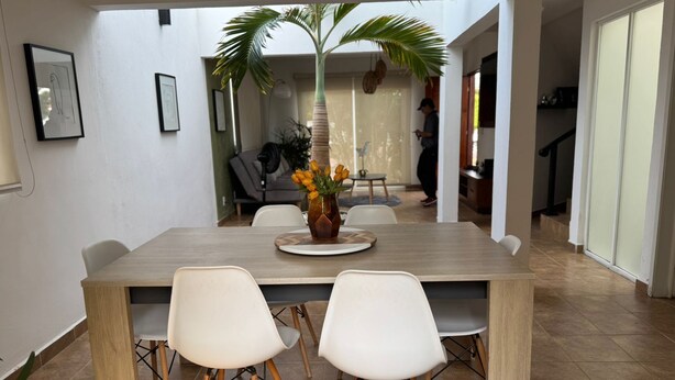 A dining area with a wooden table, four white chairs, and a vase with yellow flowers. - Casas Arrecife (Ixtapa)