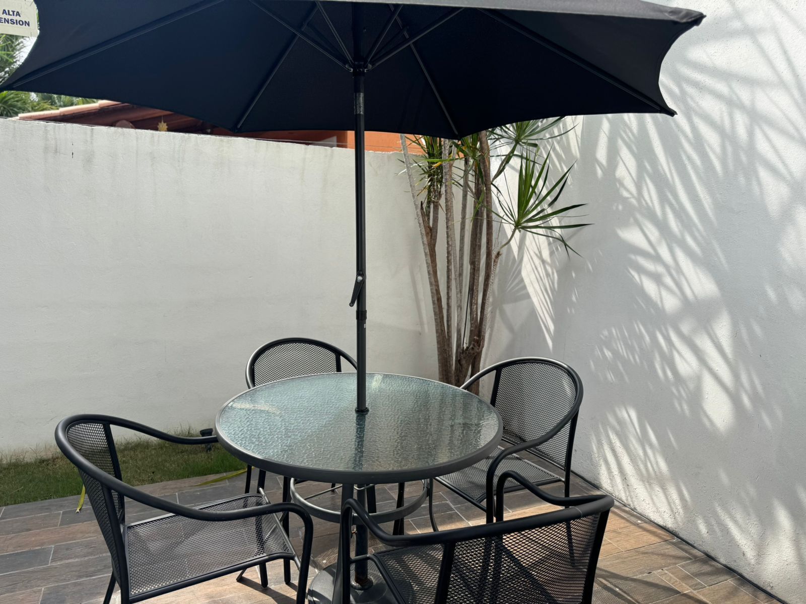A round glass table with four black metal chairs and a large black umbrella.
