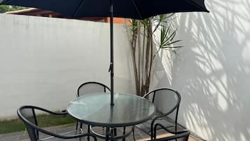 A round glass table with four black metal chairs and a large black umbrella.