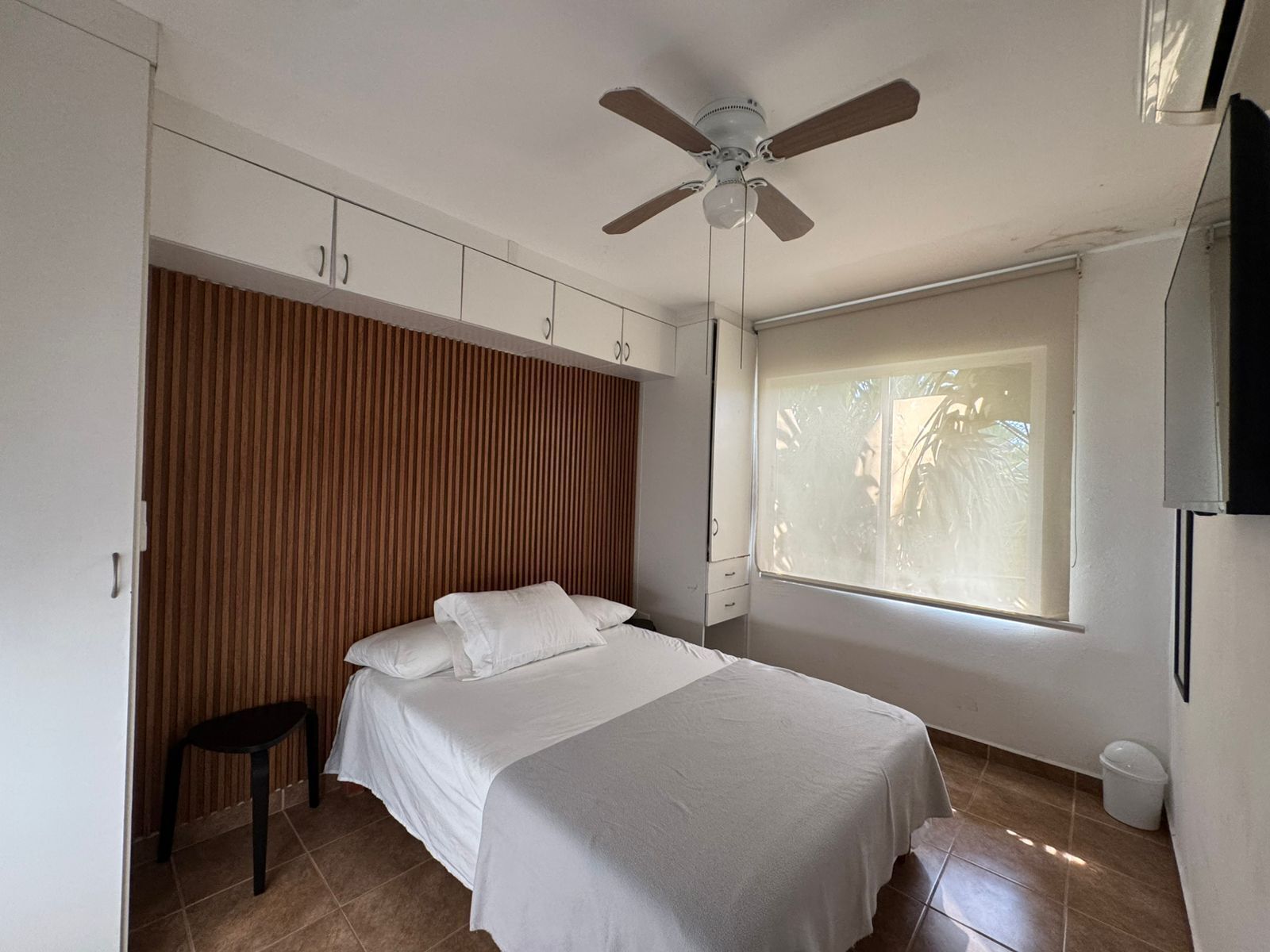 Ein Schlafzimmer mit einem Bett, Deckenventilator, Fenster und Kleiderschrank.