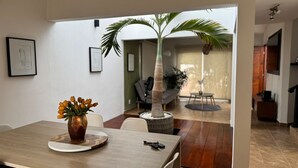 A dining area with a wooden table, chairs, a vase of flowers, and a potted palm tree. - Casas Arrecife (Ixtapa)