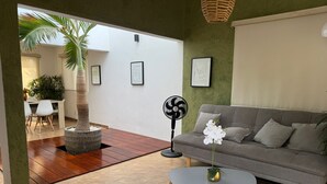 A living room with a grey sofa, a small round table, a fan, a potted plant, and a tiled floor. - Casas Arrecife (Ixtapa)