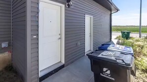 Un edificio con dos puertas blancas, un bote de basura con la leyenda 'City of Saskatoon' y una calle al fondo.
