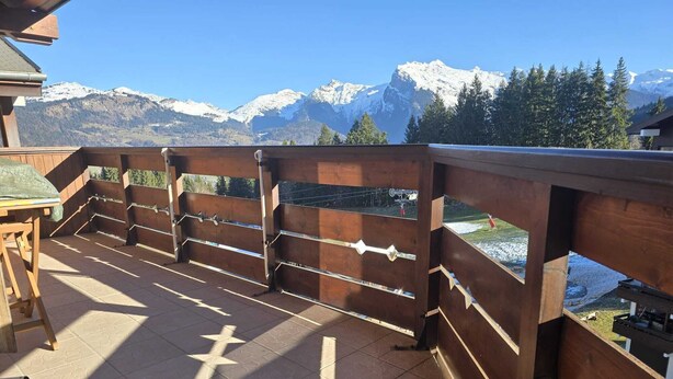 A wooden balcony with a view of snow-capped mountains. - Bright 6/7-bed apartment near town center and ski lifts (Morillon)