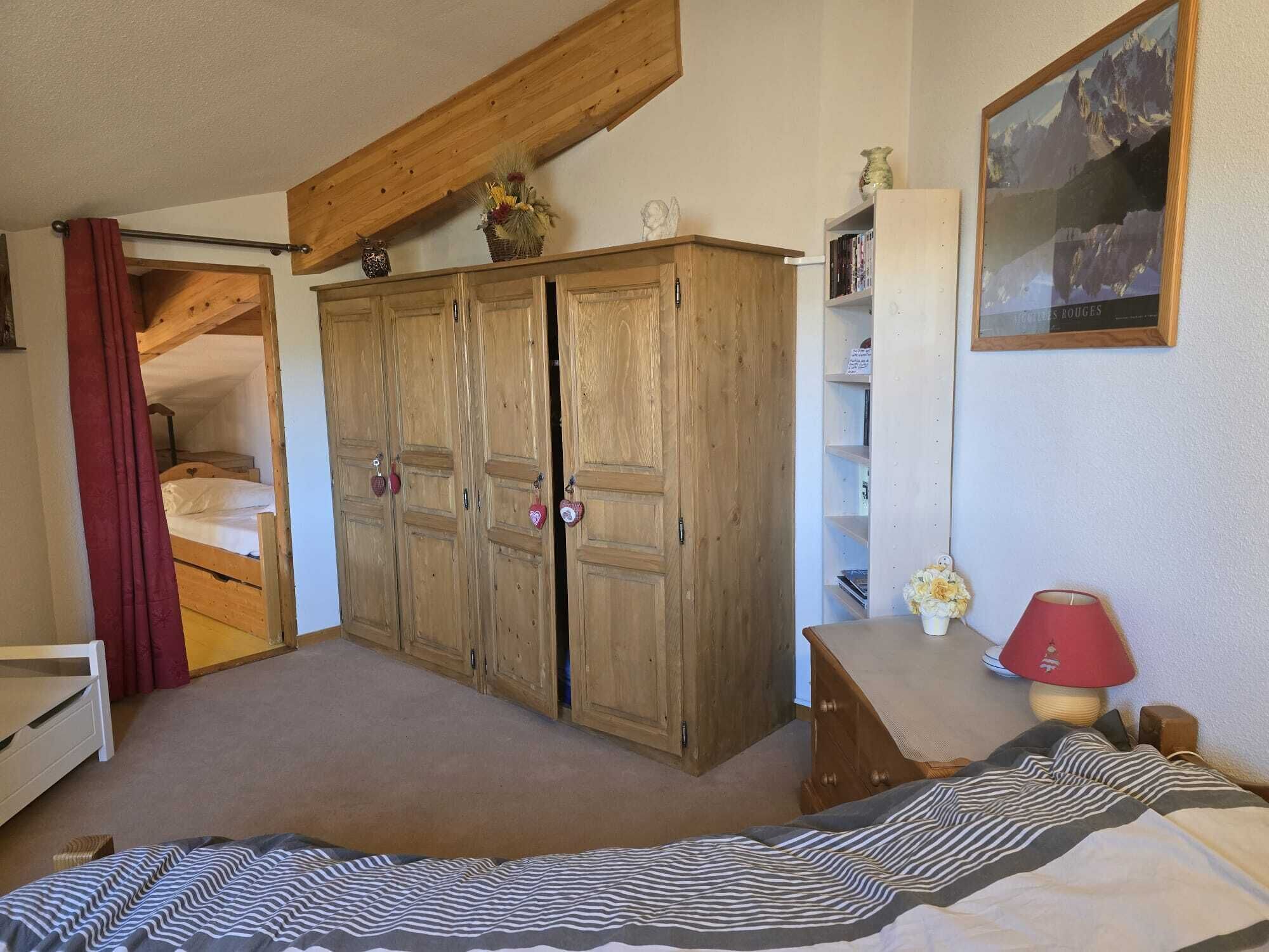 Een slaapkamer met een houten garderobe, een bed met een gestreept dekbed, een rode lamp en een ingelijst beeld aan de muur.
