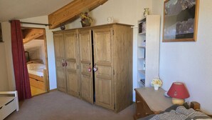 A bedroom with a wooden wardrobe, a bed with a striped blanket, a red lamp, and a framed picture on the wall. - Bright 6/7-bed apartment near town center and ski lifts (Morillon)