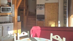 A cozy kitchen with a microwave, stove, and wooden cabinets. There's a dining area with a table and chairs, and a clock on the wall. - Bright 6/7-bed apartment near town center and ski lifts (Morillon)