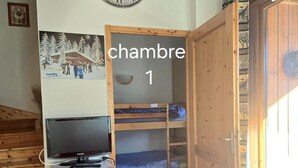 A room with bunk beds, a wooden cabinet with a television, a wall clock, and a door labeled "chambre 1". - Bright 6/7-bed apartment near town center and ski lifts (Morillon)