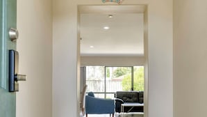 Un pasillo que conduce a una sala de estar con un sofá y una silla, un adorno colgante y una puerta con picaporte.