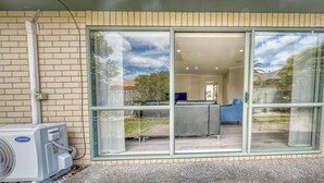 Casa con fachada de ladrillo, puerta corrediza de vidrio que da a un patio con un sofá gris y una silla azul, y un equipo de aire acondicionado a la izquierda.