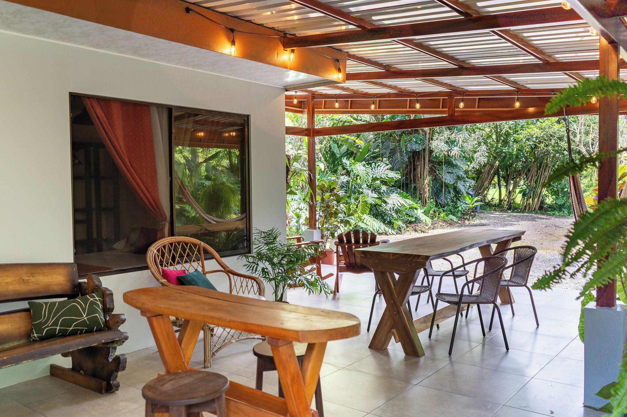 An outdoor patio area with wooden furniture, including a table and chairs, and a pergola with string lights.