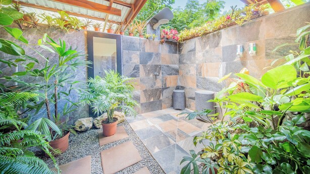 A covered outdoor area with stone walls, potted plants, and a built-in shower. - Hummingbird jungle (La Fortuna)