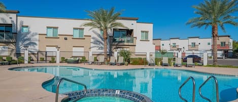A swimming pool with a hot tub, surrounded by palm trees and modern buildings.