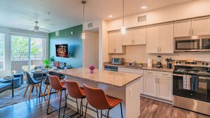 A modern kitchen with white cabinets, a large island with bar stools, a microwave, and an oven. - Walk To Stadium with Balcony-Pool-Gym-Parking-W/D (Glendale)