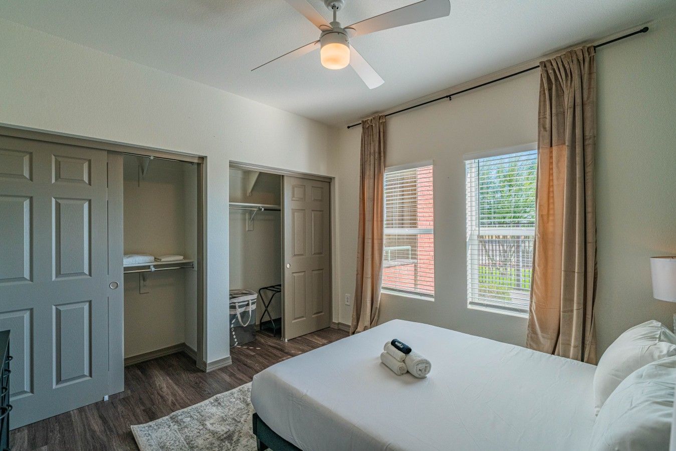A bedroom with a bed, a ceiling fan, a window with curtains, and a closet.