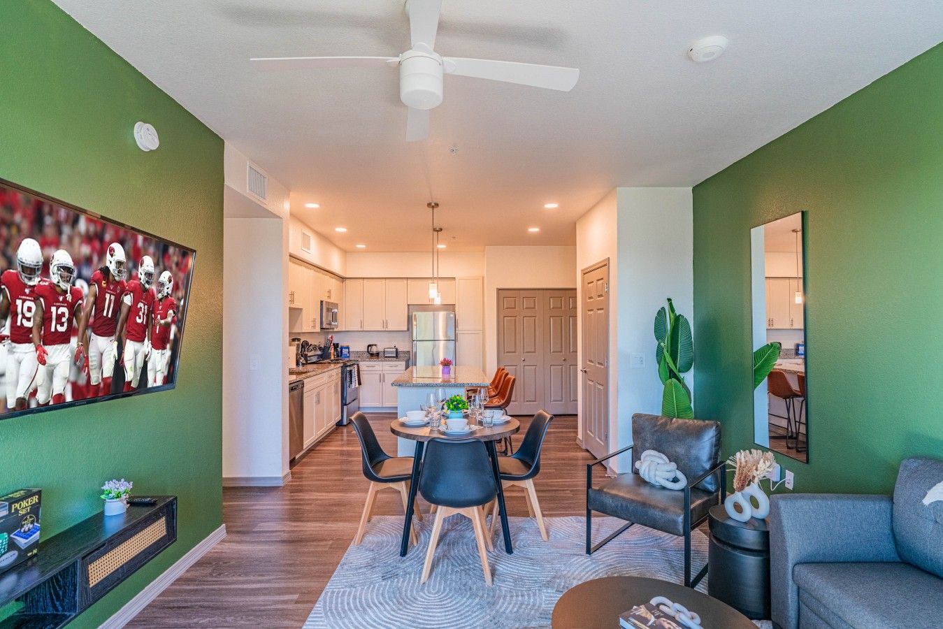 A modern living room with a dining area, a kitchen in the background, and a large sports-themed wall art.