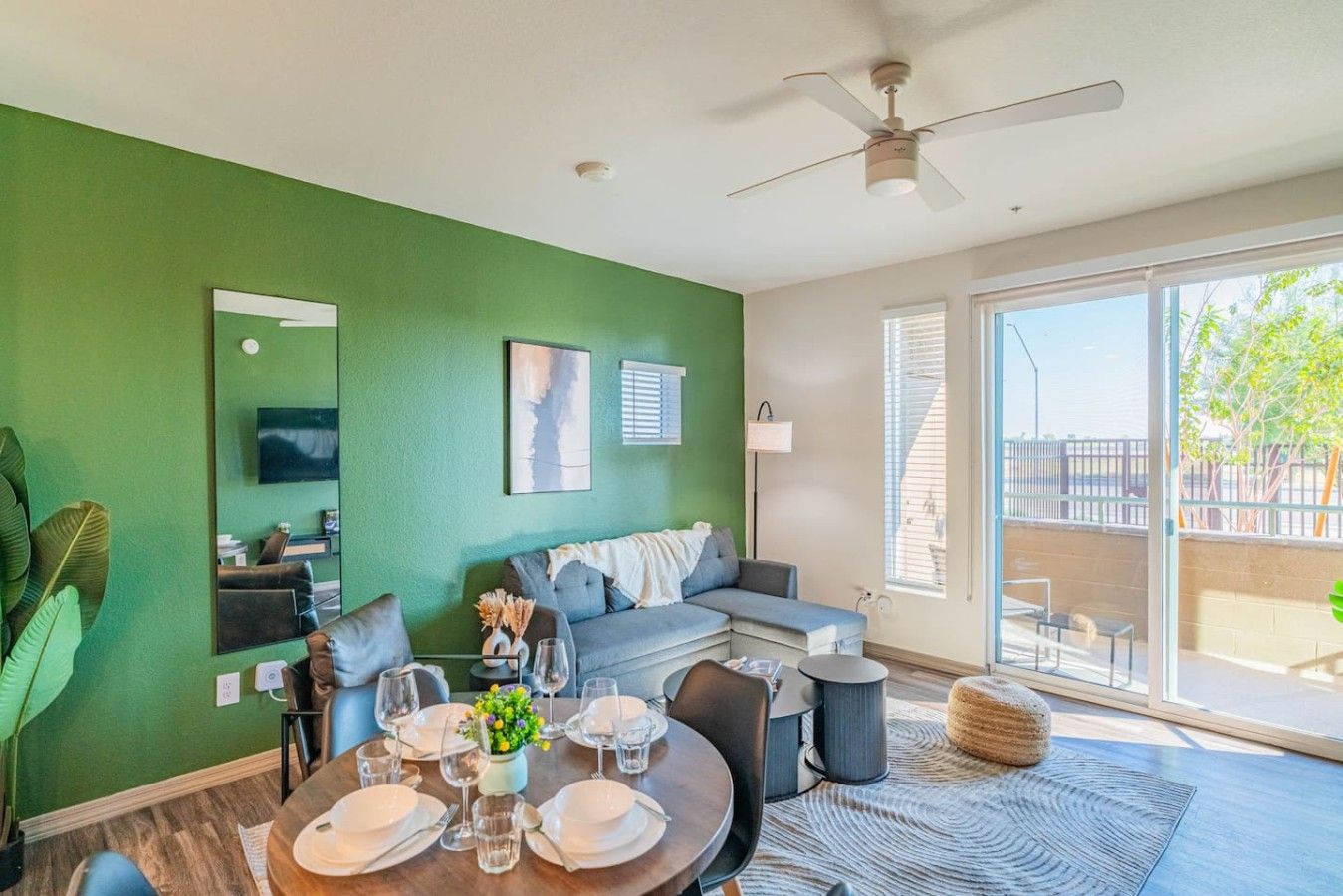 Un coin repas avec une table dressée pour quatre personnes, un canapé, un ventilateur de plafond et une grande fenêtre donnant sur l’extérieur.