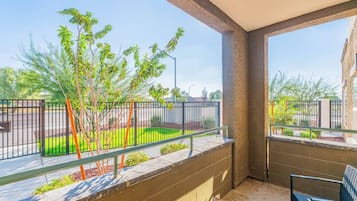 Un balcón con vista a un jardín ajardinado, barandilla metálica y una silla.