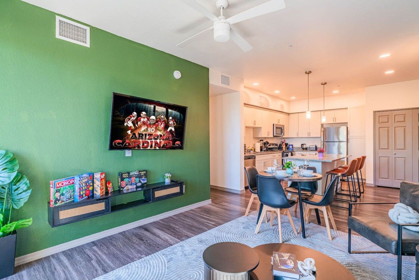 Un salon moderne avec un mur d’accent vert, un téléviseur fixé au mur et un coin repas comprenant une table et des chaises.