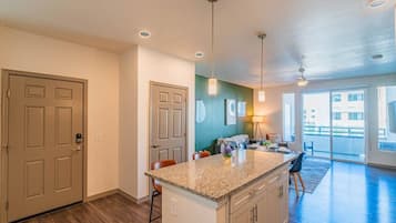 A modern kitchen with a granite countertop, a dining area with a table and chairs, and a view of the outside through a sliding glass door.