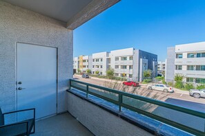 A balcony with a view of modern apartment buildings, a street with cars, and a clear blue sky.