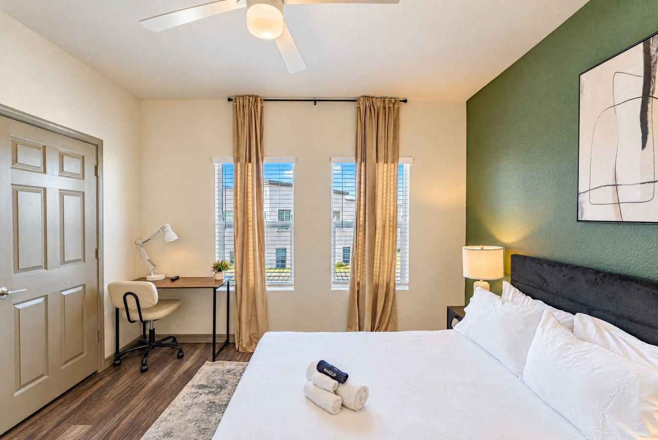 Ein Hotelzimmer mit Bett, Schreibtisch, Stuhl und Blick auf Gebäude durch das Fenster.