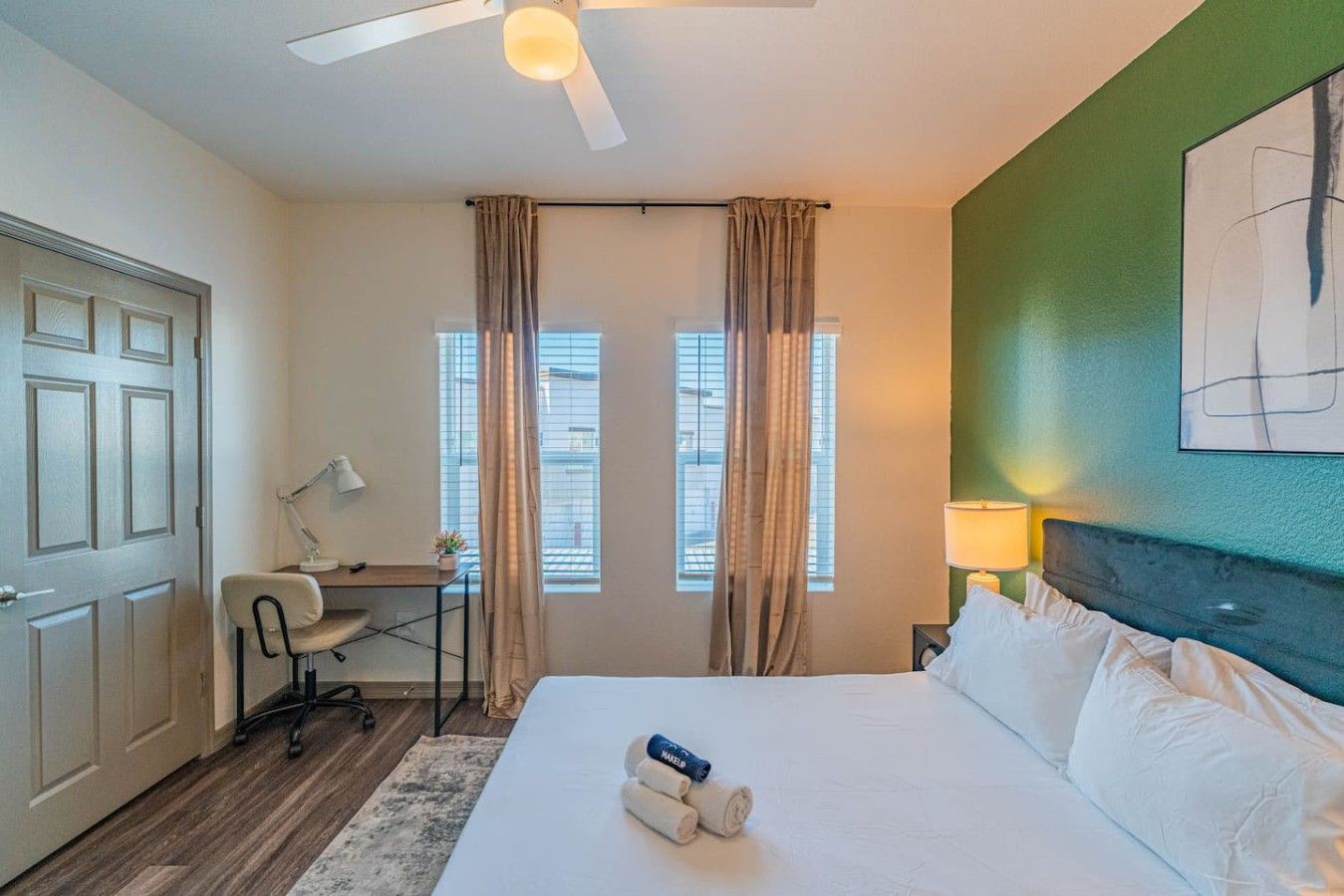 A hotel room with a bed, desk, chair, and a ceiling fan.