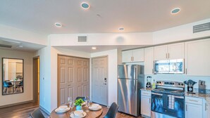 A modern kitchen with stainless steel appliances, a dining area with a round table and chairs, and a separate dining room visible through an open door. - Stadium Area Unit w/ Balcony,Pool,Gym,Parking,W/D (Glendale)