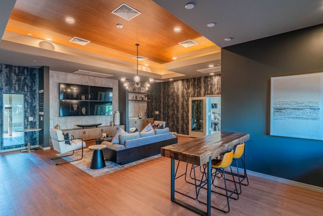 A modern interior with a wooden ceiling, a dining area with bar stools, a sofa, and a kitchen with built-in shelves.