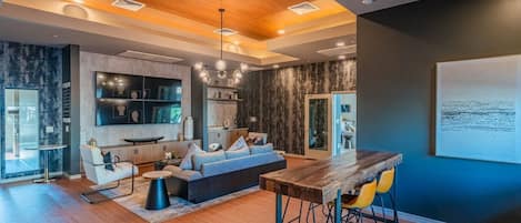 A modern interior with a wooden ceiling, a dining area with bar stools, a sofa, and a kitchen with built-in shelves.