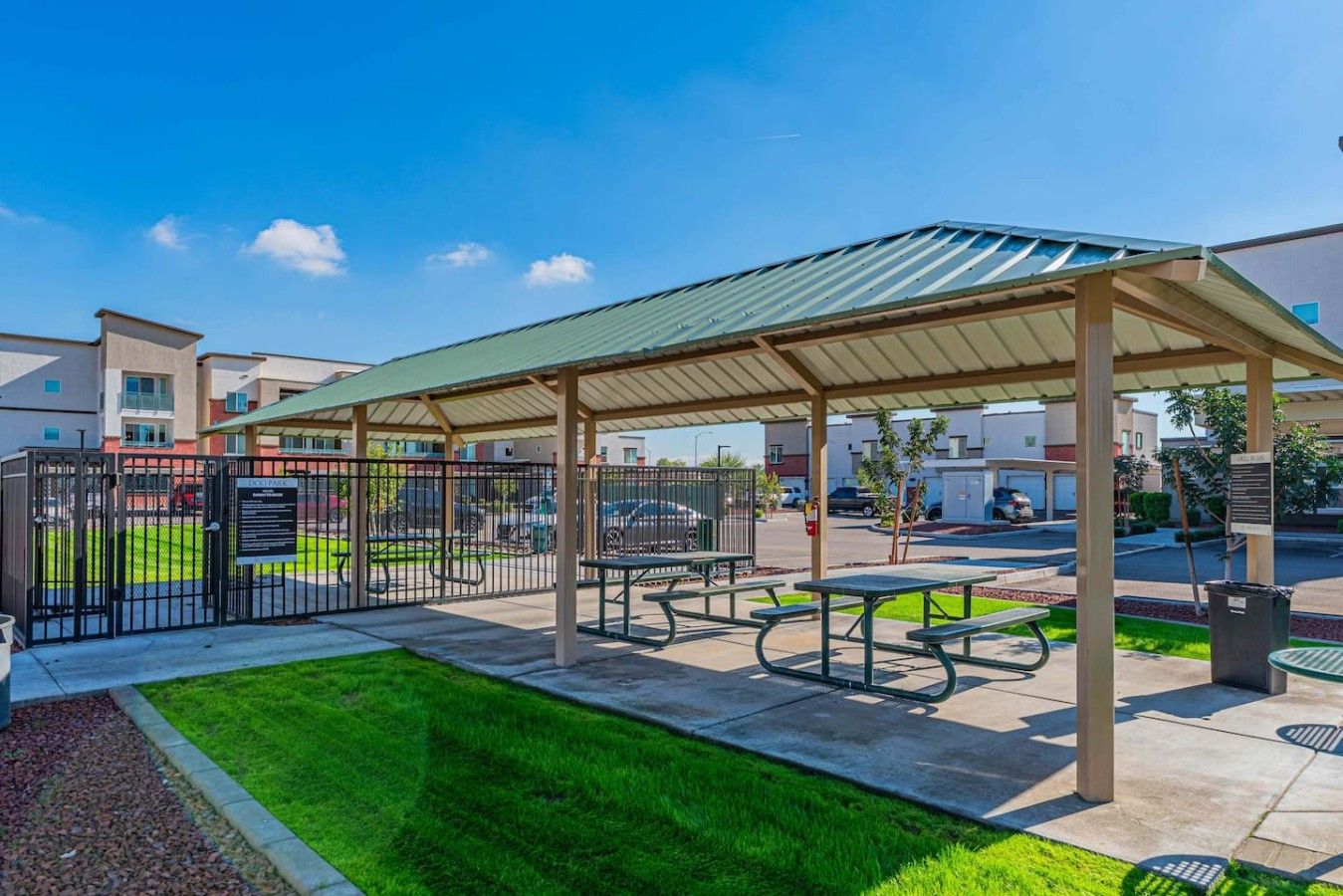 A covered outdoor seating area with picnic tables and a fenced parking lot.