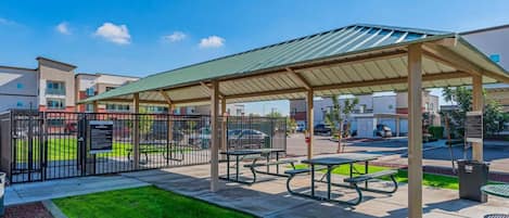 A covered outdoor seating area with picnic tables and a fenced parking lot.
