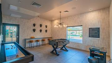 A room with a foosball table, bar stools, and a foosball table with a view of the outside.