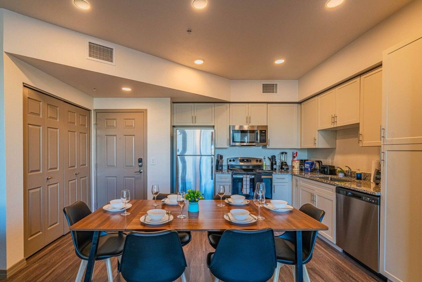 A modern kitchen with white cabinets, a stainless steel refrigerator, and a dining area with a wooden table set for four.