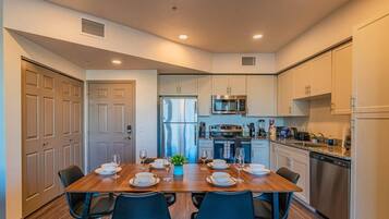 A modern kitchen with white cabinets, a stainless steel refrigerator, and a dining area with a wooden table set for four.