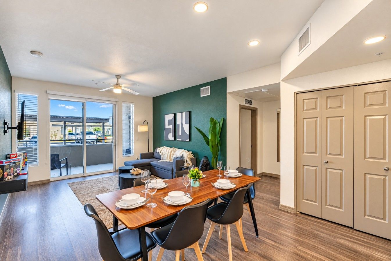 A modern dining area with a wooden table set for four, a sofa, and a view of the outdoors.