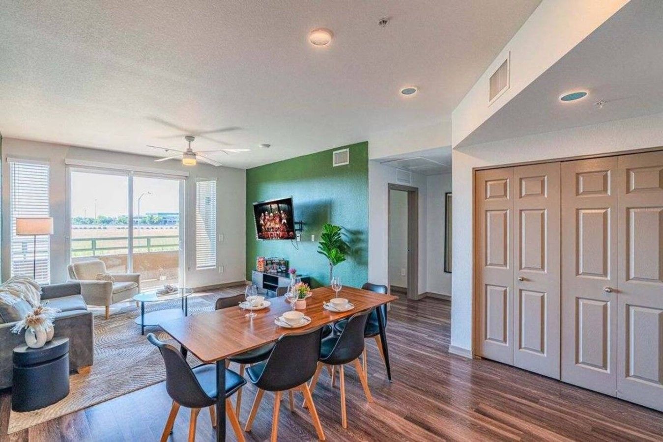 A dining area with a wooden table and chairs, a ceiling fan, and a green accent wall.