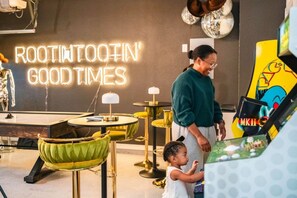 Un intérieur moderne avec un panneau néon sur lequel on peut lire « AMUSEZ-VOUS BIEN », un enfant interagissant avec un distributeur automatique et une femme se tenant à proximité.