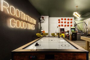 A billiards table with a neon sign reading 'ROOT INTO GOOD TIMES' in a room with a green ceiling, a basketball arcade, and a wall with orange basketballs. - HeatedPool PickleBall Basktball Golf FirePit Games (San Antonio)