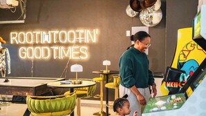 A neon sign reading "ROOTIN' TOOTIN' GOOD TIMES" in a modern interior with round tables and chairs. - HeatedPool PickleBall Basktball Golf FirePit Games (San Antonio)