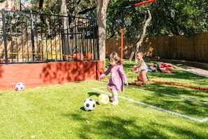 A child playing soccer in a fenced outdoor area with grass and trees in the background. - HeatedPool PickleBall Basktball Golf FirePit Games (San Antonio)
