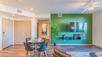 A modern living room with a dining area, a green accent wall, a ceiling fan, and a mounted TV.