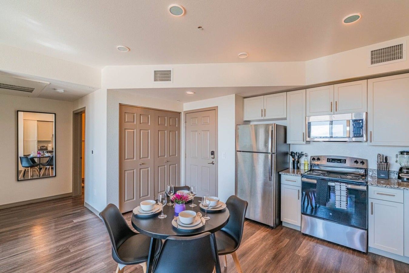 A modern kitchen with stainless steel appliances, a dining area with a table set for four, and a hallway leading to another room.