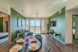 A dining area with a table set for four, a sofa, and a television mounted on the wall. - Spot Near Westagate w/Balcony,Pool,Gym,Parking,W/D (Glendale)