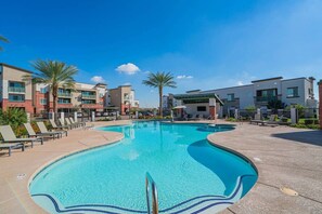 A swimming pool with lounge chairs and a covered seating area, surrounded by modern buildings. - Spot Near Westagate w/Balcony,Pool,Gym,Parking,W/D (Glendale)