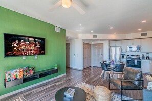 A modern living room with a flat-screen TV, a dining area with chairs, a kitchen with appliances, and a hallway. - Spot Near Westagate w/Balcony,Pool,Gym,Parking,W/D (Glendale)