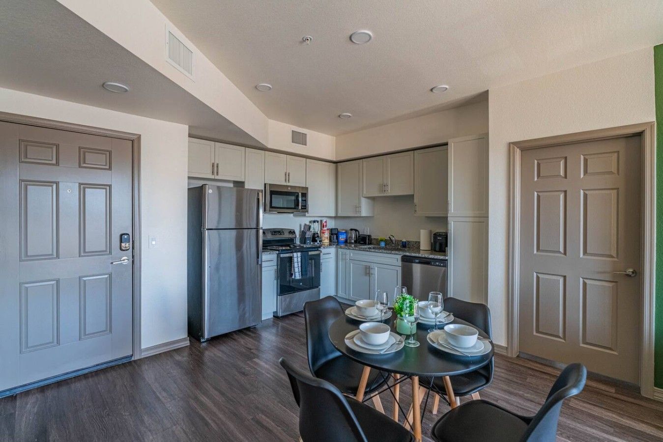 A modern kitchen with stainless steel appliances, a dining area with a table set for four, and a large window providing natural light.